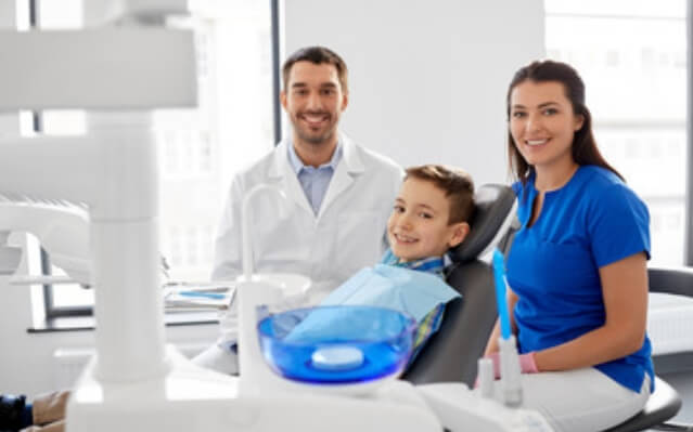 Dentist dental team member and young patient in dental treatment room