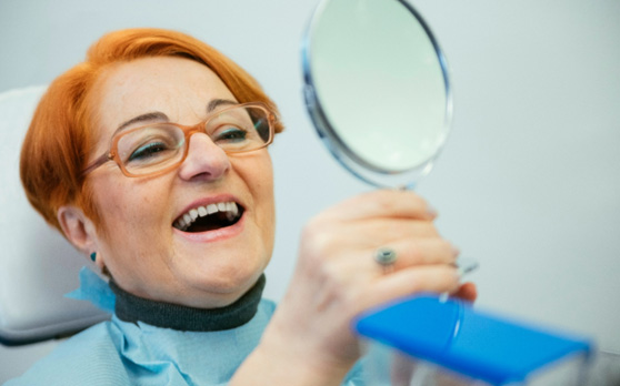 An older woman admiring her new dentures with a hand mirror