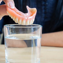 Someone placing dentures in a glass of solution