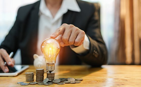 Man tapping a lightbulb that’s on top of a stack of coins