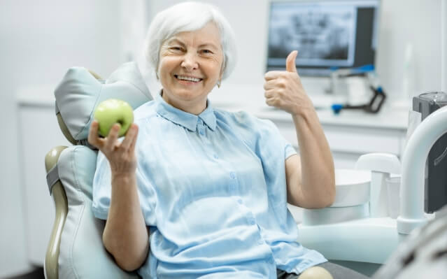 Woman smiling and holding an apple after dental implant tooth replacement