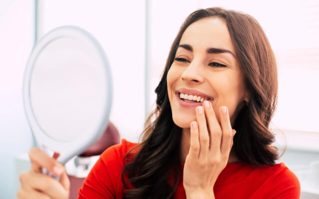 Woman looking at smile after dental implant tooth replacement