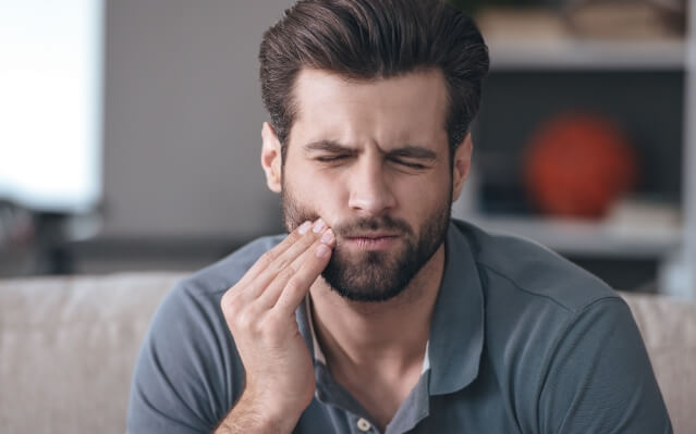 Man in need of emergency dentistry holding cheek in pain