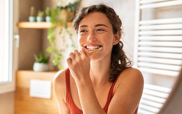 Woman in bathroom brushing her teeth and smiling