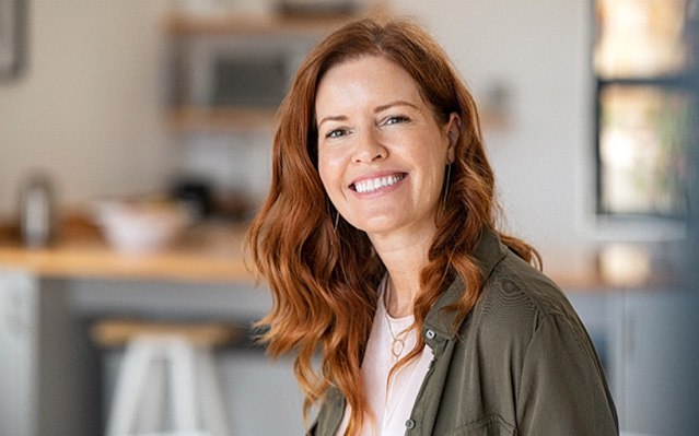 Woman with green jacket standing at home and smiling