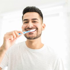 Man with white shirt brushing his teeth 