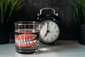 Set of dentures in a glass of water next to a clock