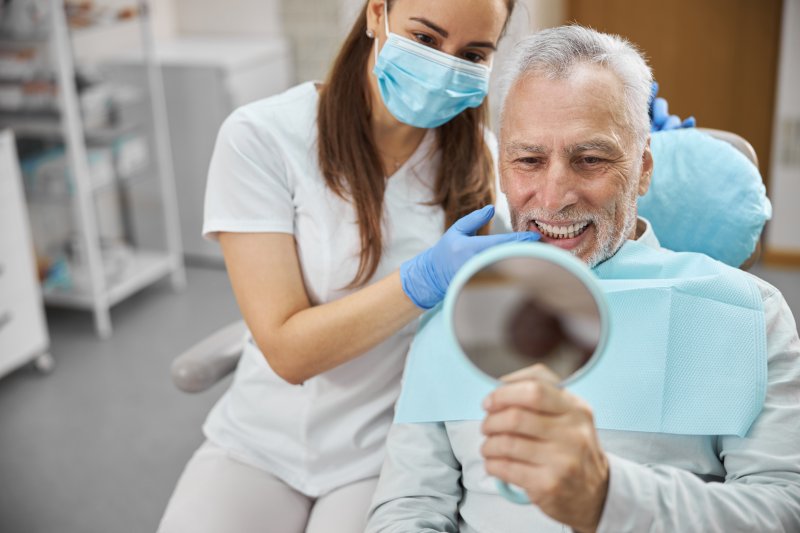 An older man admiring his dental implants with a hand mirror
